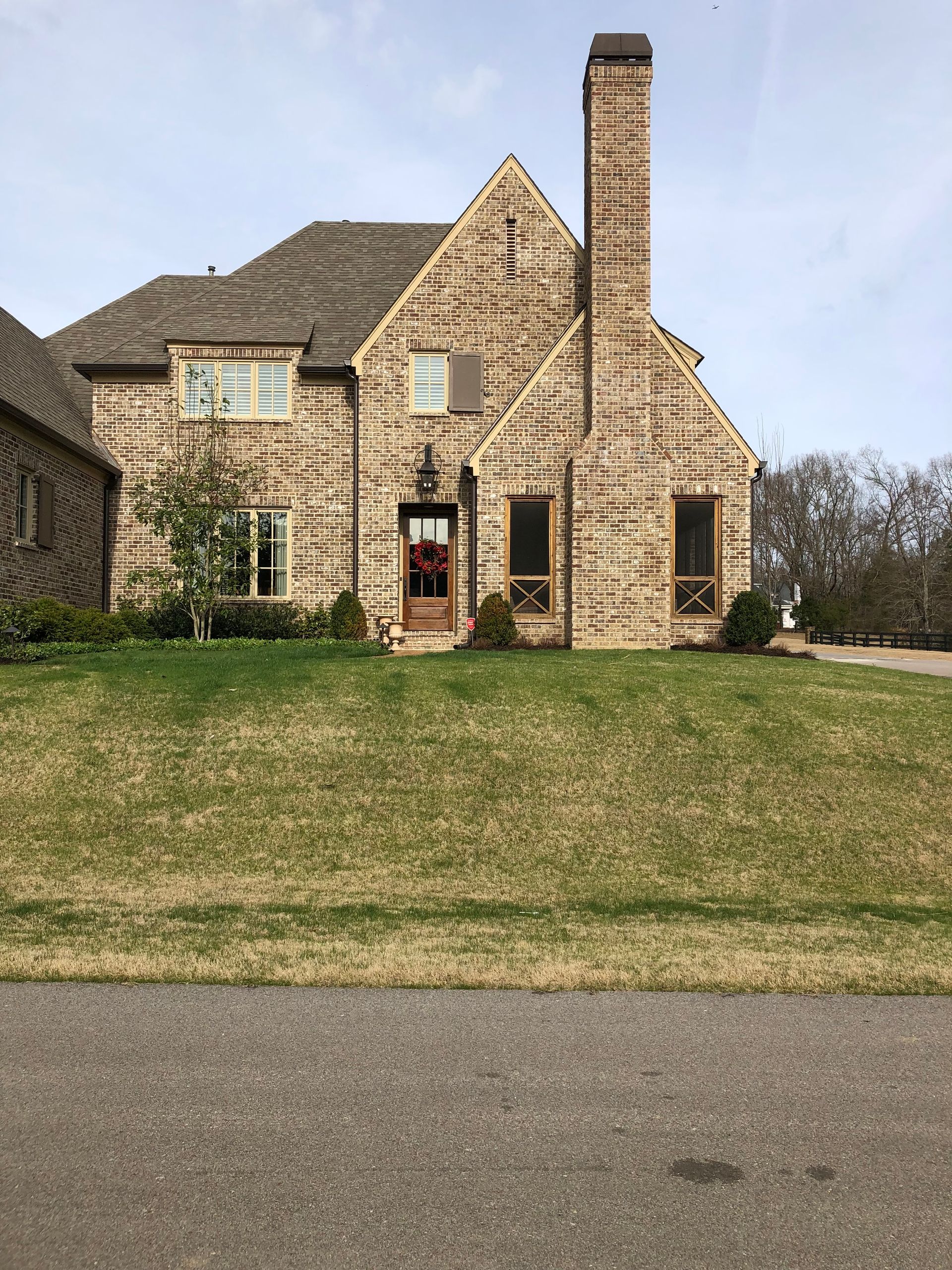 Two-story brick house with a tall chimney, brown roof, and a green lawn.