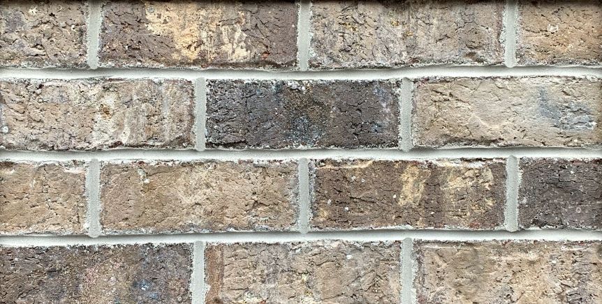 Close-up of a brick wall with varied brown and tan bricks and gray mortar.