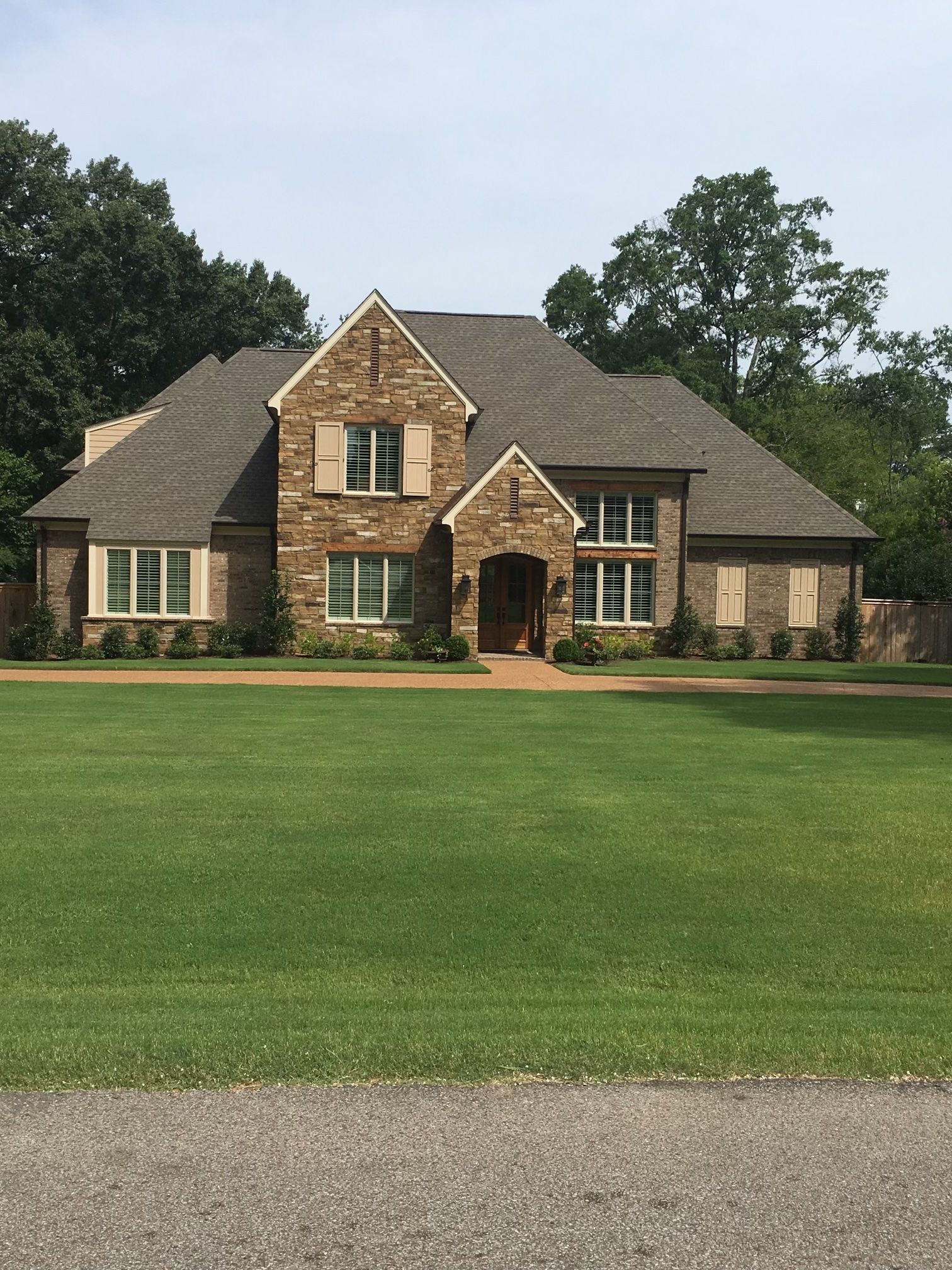 Brick house with a green lawn, surrounded by trees, under a blue sky.