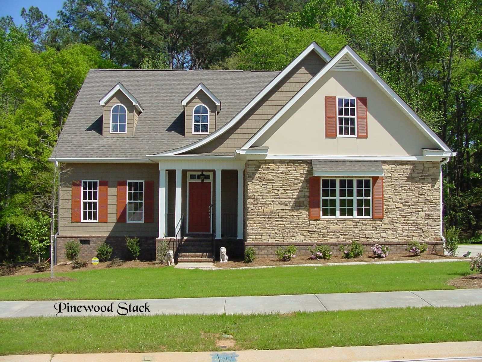 A single-story house with stone facade, red door, brown shutters, and green lawn.