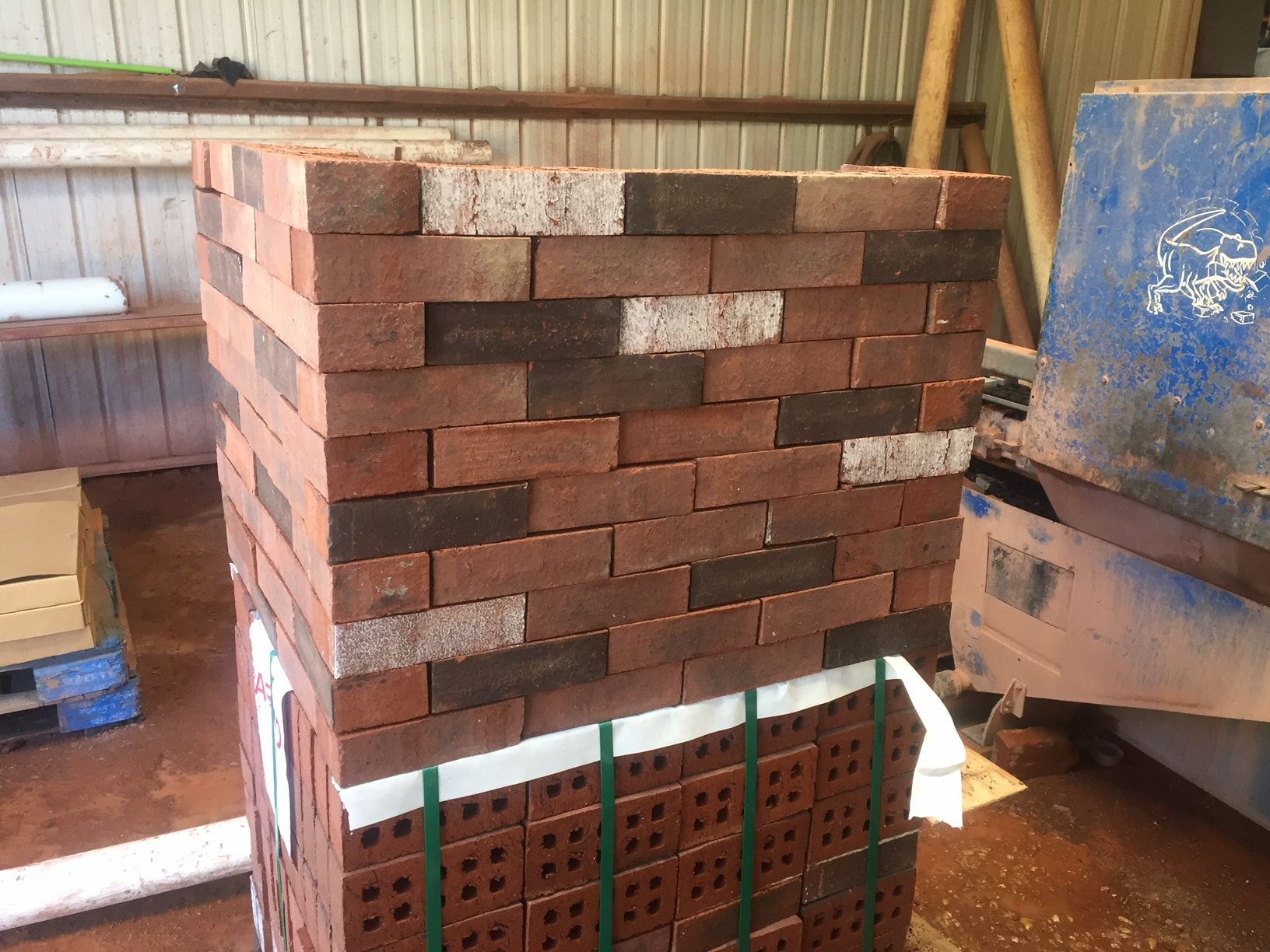 A stack of red bricks bundled together with green straps in a warehouse setting.