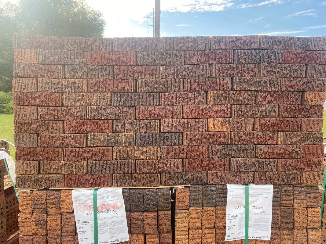 Stacked red bricks, bound with green straps, outdoors under a blue sky.