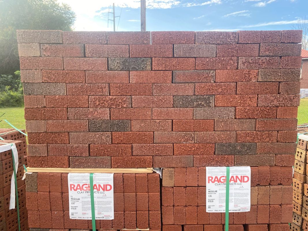 Stack of reddish-brown bricks, some with darker tones, bundled together with straps, labeled 