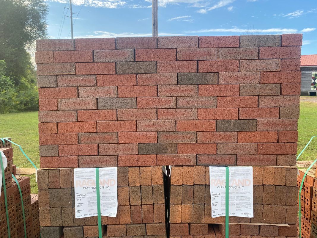 Stack of red and brown bricks, outdoors on a grassy area, ready for construction.