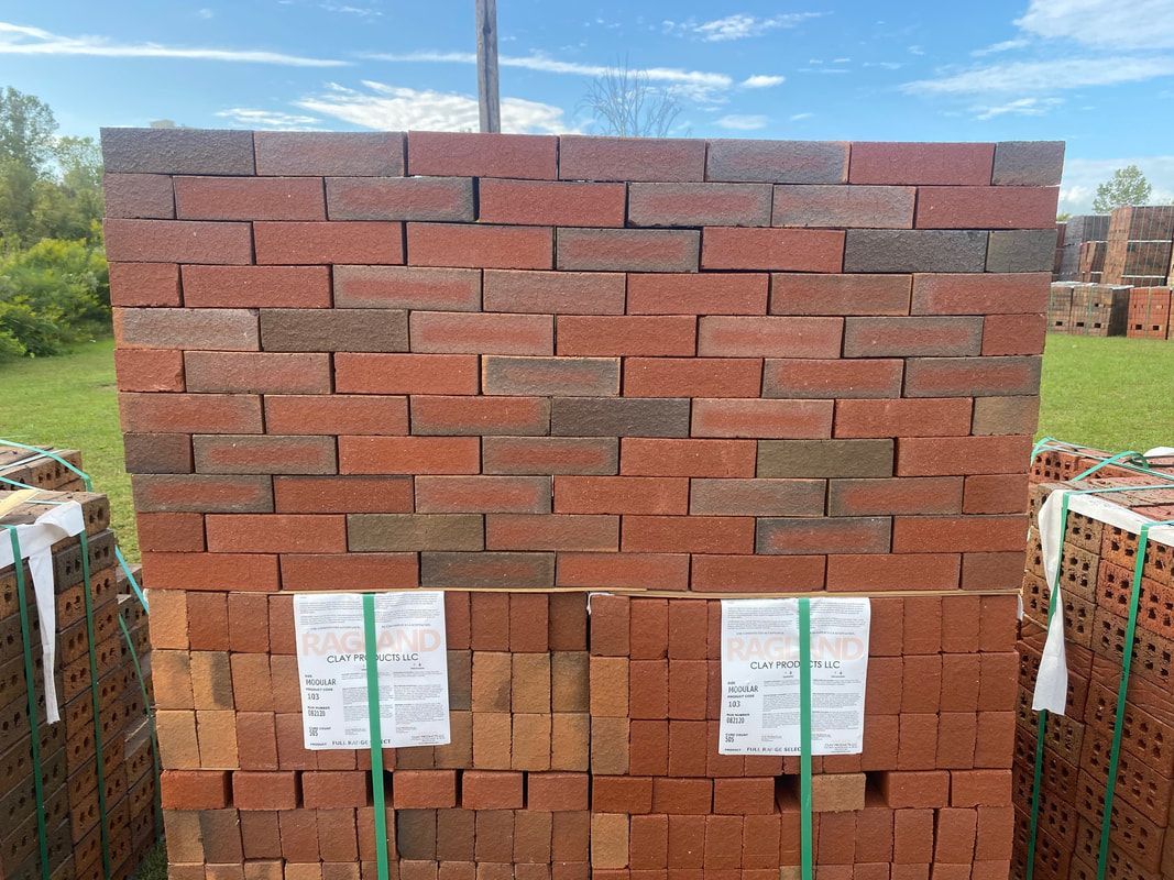 A stack of red and brown bricks, outdoors on a sunny day. Paper tags attached to lower portion.