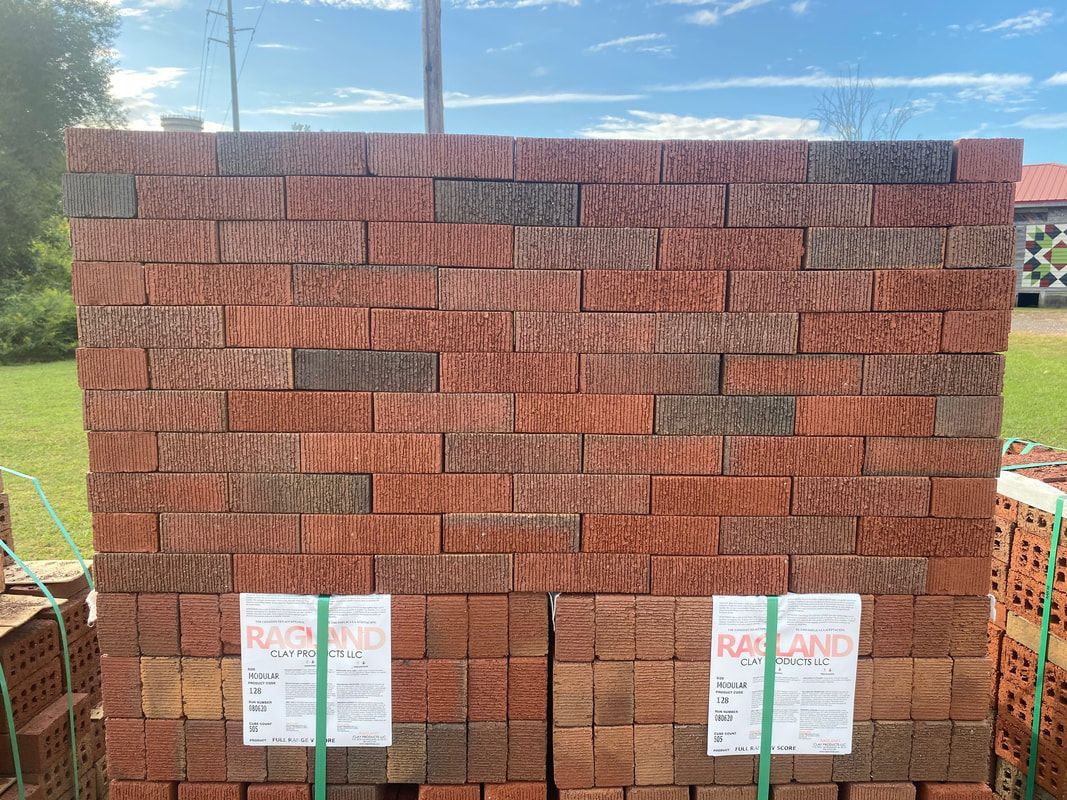 Stack of reddish-brown bricks, some with darker tones, bundled together with green straps outdoors.