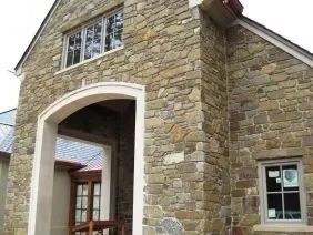 Stone facade of a house with archway, windows, and angled roof.