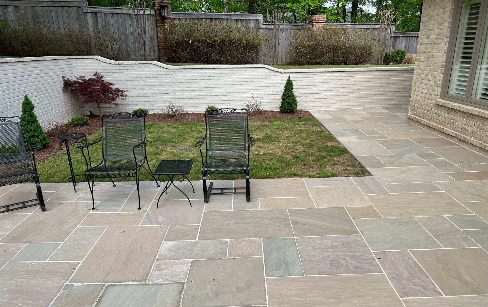 Patio with flagstone pavers, chairs, and small lawn area near a building and fence.