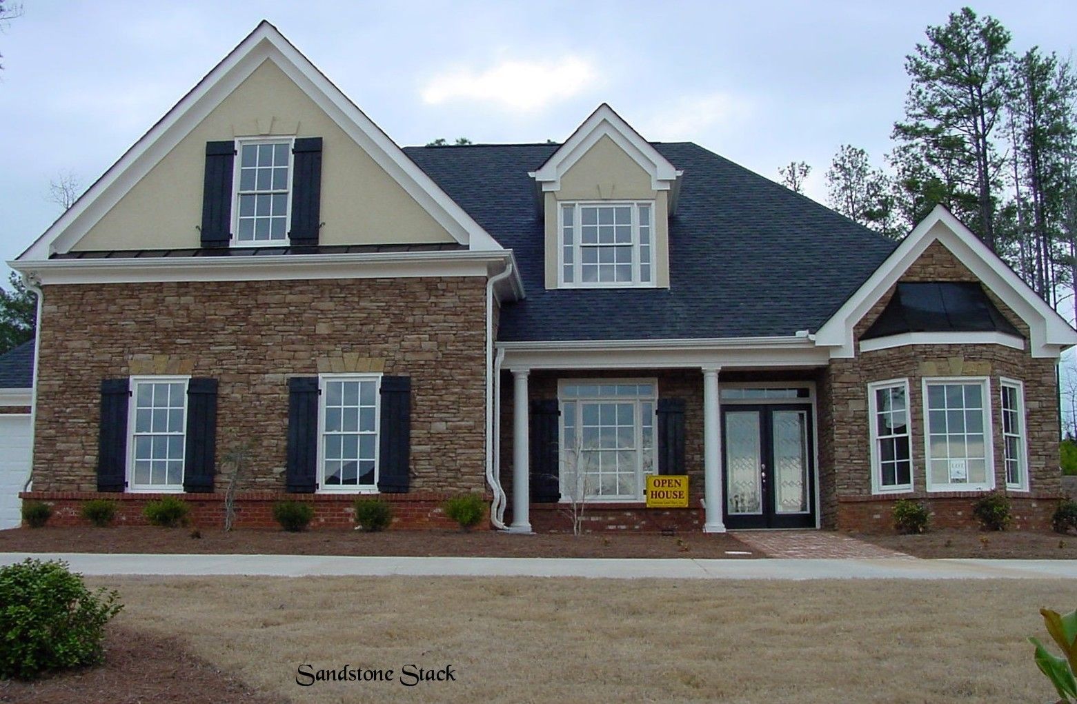 A two-story house with brick and stone facade, black shutters, and a dark roof.