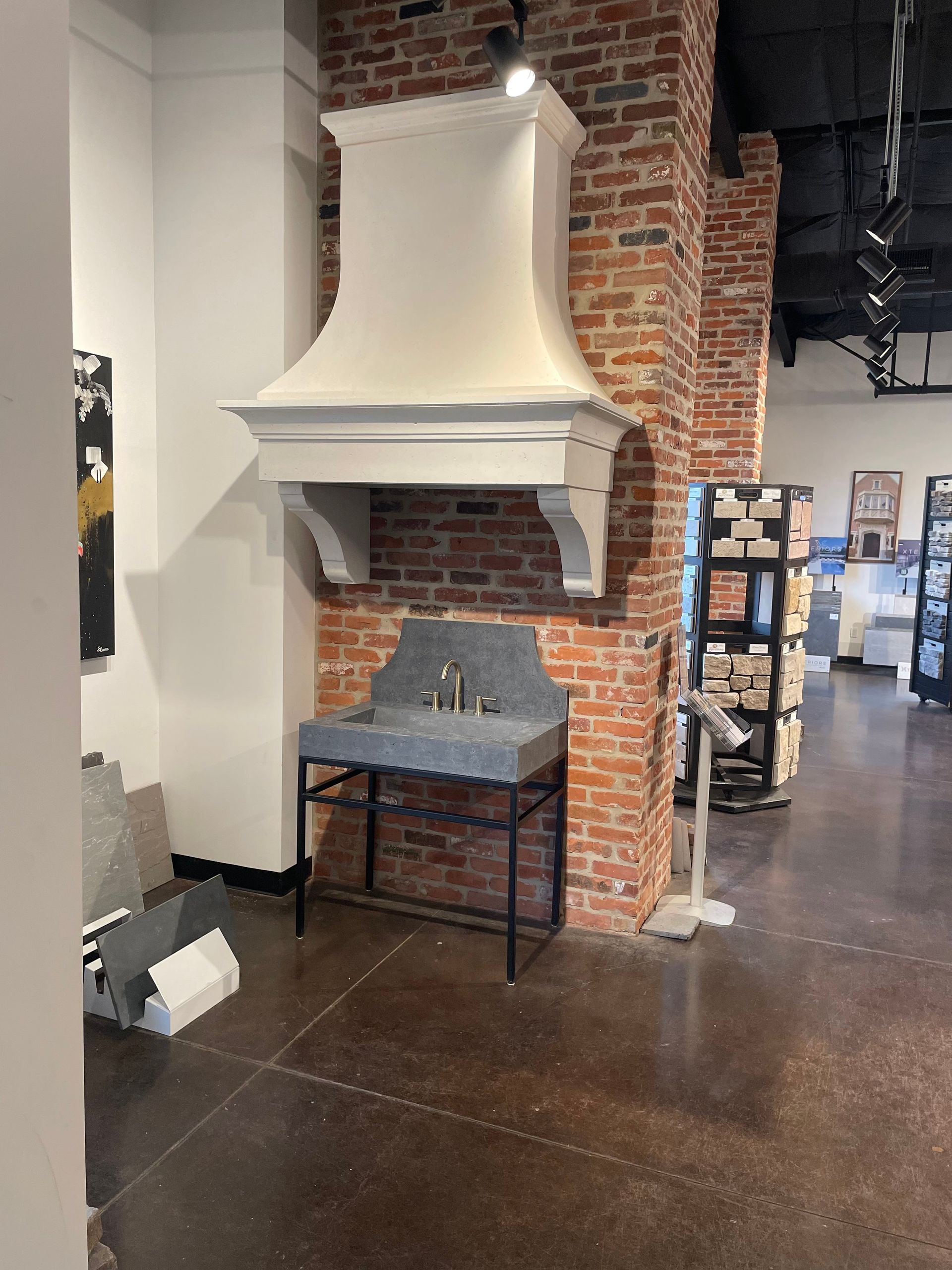 White range hood above a gray sink with black metal legs set against a brick pillar.