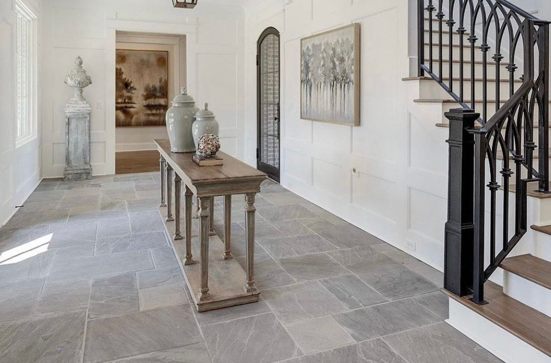 Hallway with stone floor, white walls, console table with vases, and a staircase with wrought iron railing.