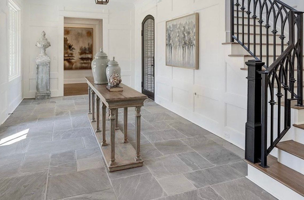 Hallway with stone floor, white walls, console table with vases, and a staircase with wrought iron railing.