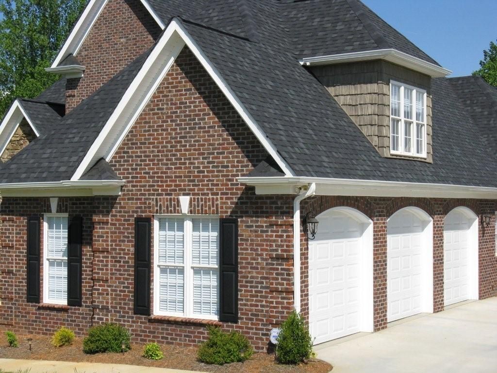 Brick house with black roof, white garage doors, shutters, and trim.
