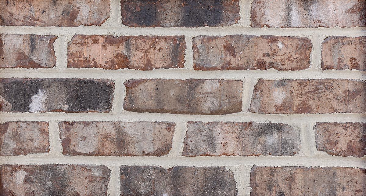 Close-up of brick wall with varying shades of brown and gray bricks, laid with light-colored mortar.