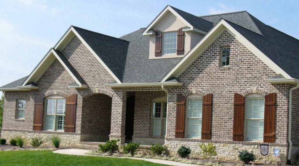 Brick house with brown shutters and a dark roof.