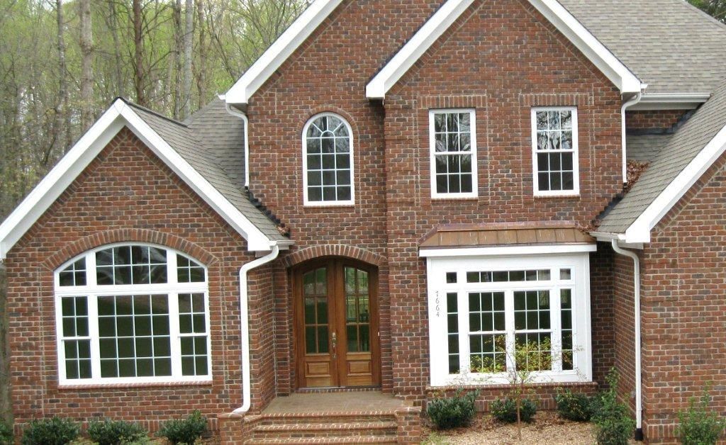 Brick house with white trim, multiple windows, and a wooden door.