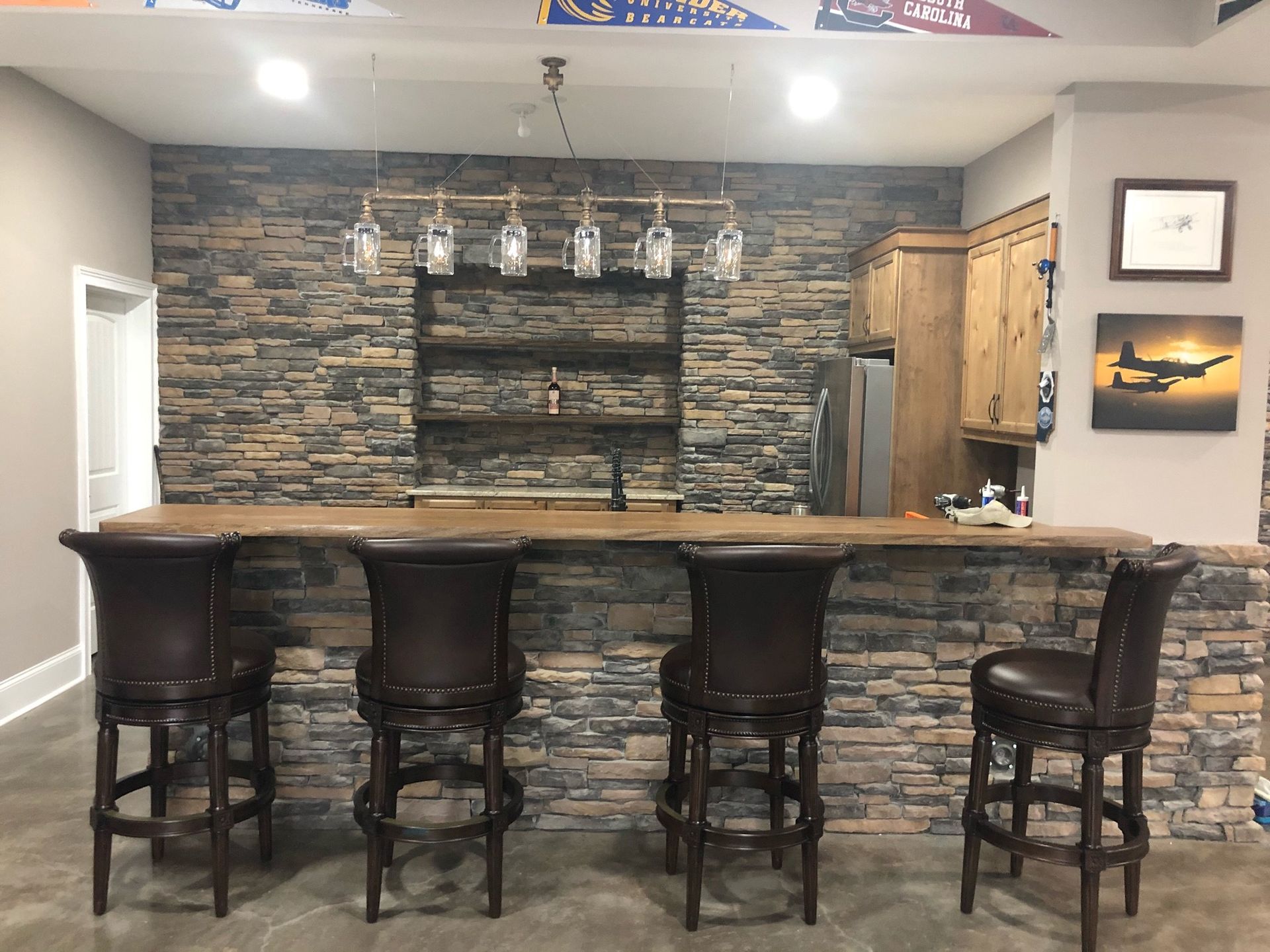 Basement bar with stone wall, wooden counter, and four brown leather bar stools.