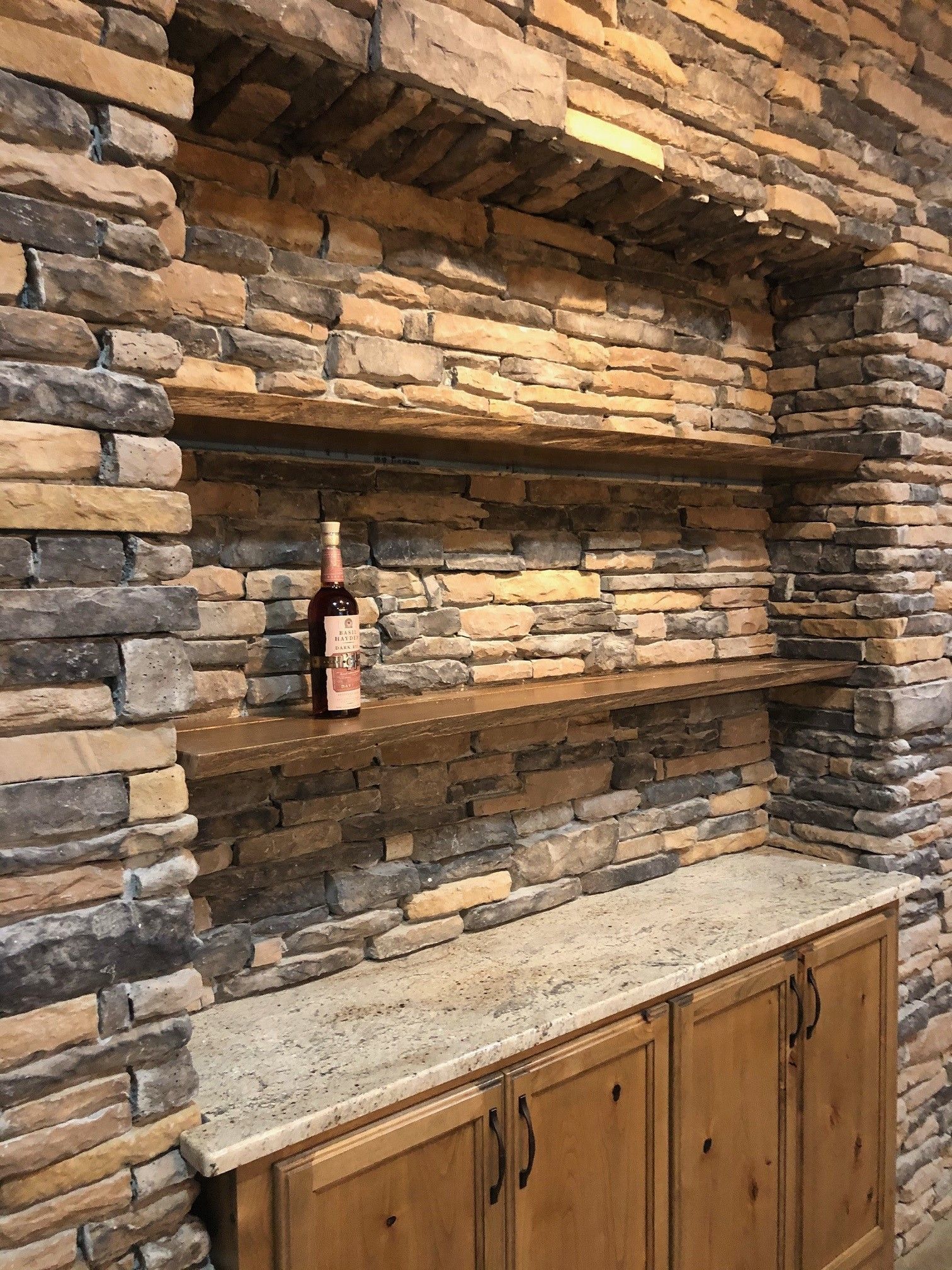 Built-in stone shelving with a bottle of wine. Wooden cabinets and a granite countertop.