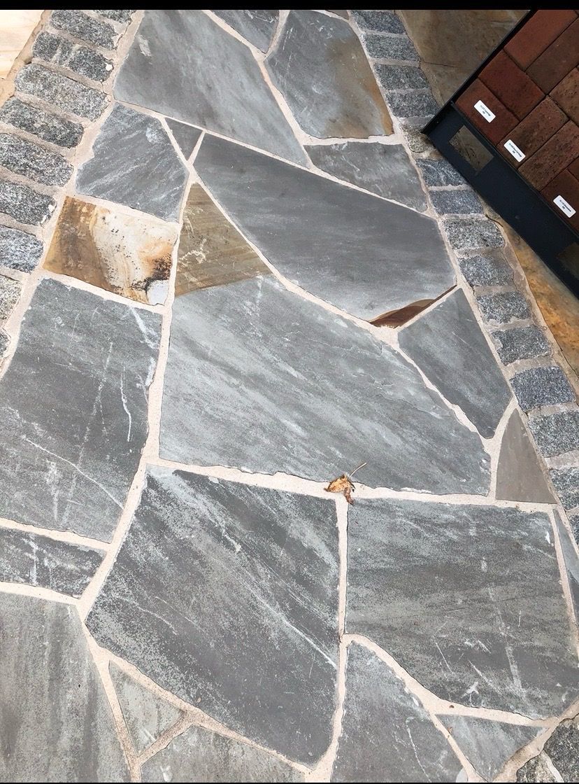 Irregular gray flagstone patio with lighter grout, bordered by brick.