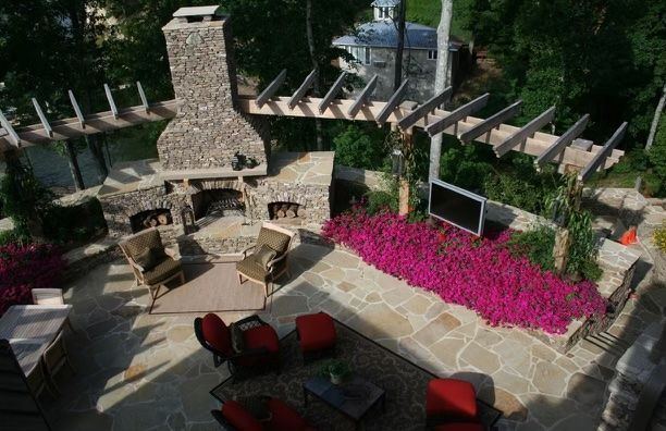 Stone patio with fireplace, seating, pergola, and bright pink flowers.