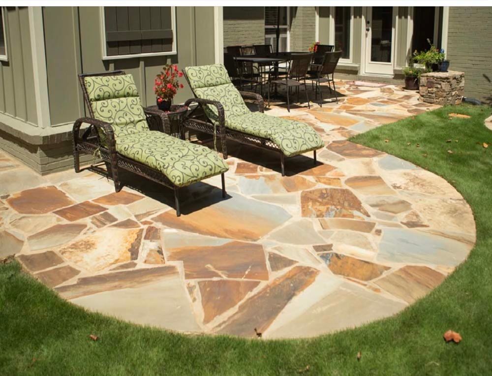 Patio with flagstone pavers, two lounge chairs, and a dining set on a green lawn.
