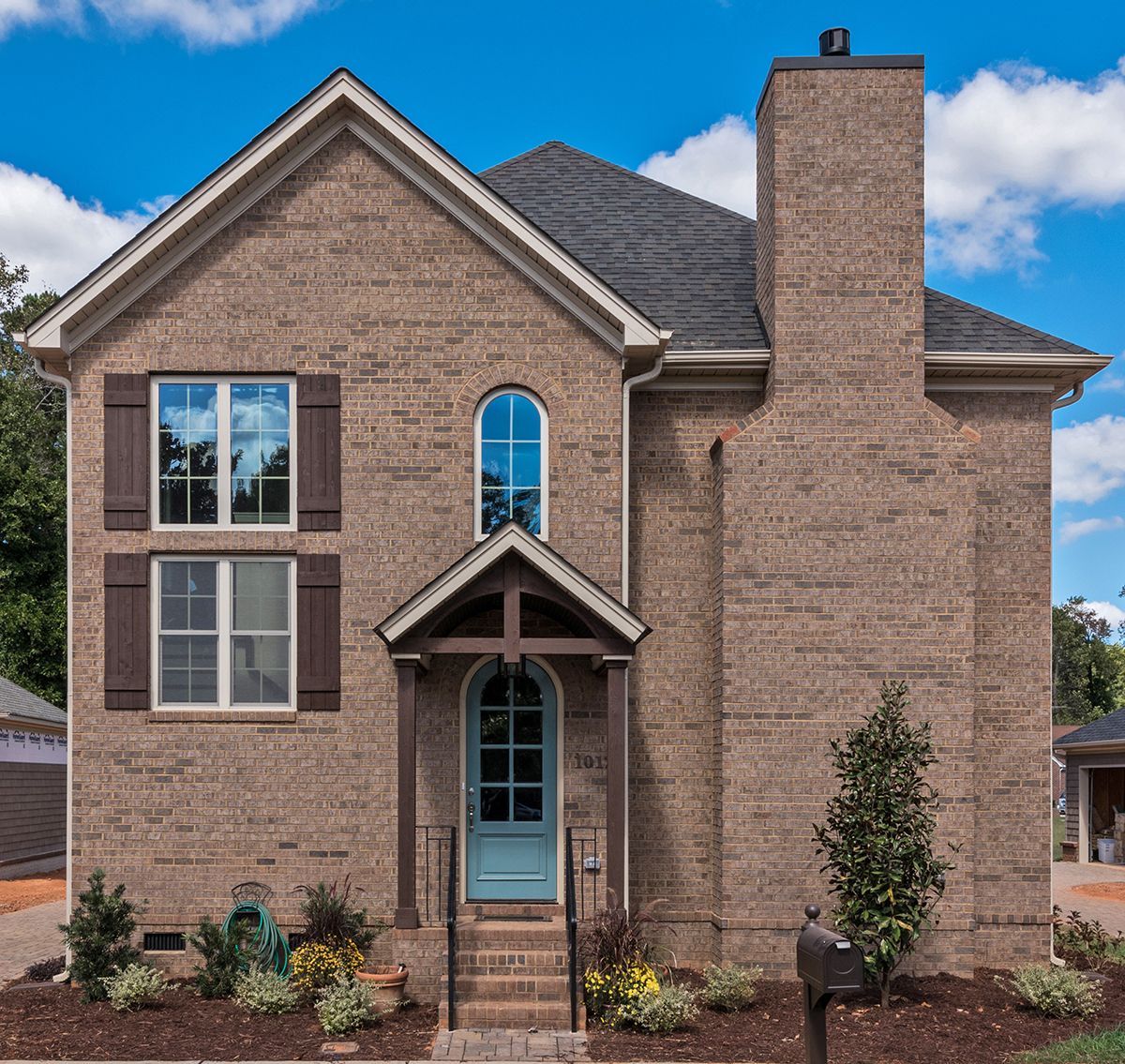 Two-story brick house with blue door and arched window under a small portico; brown shutters, chimney, and dark roof.