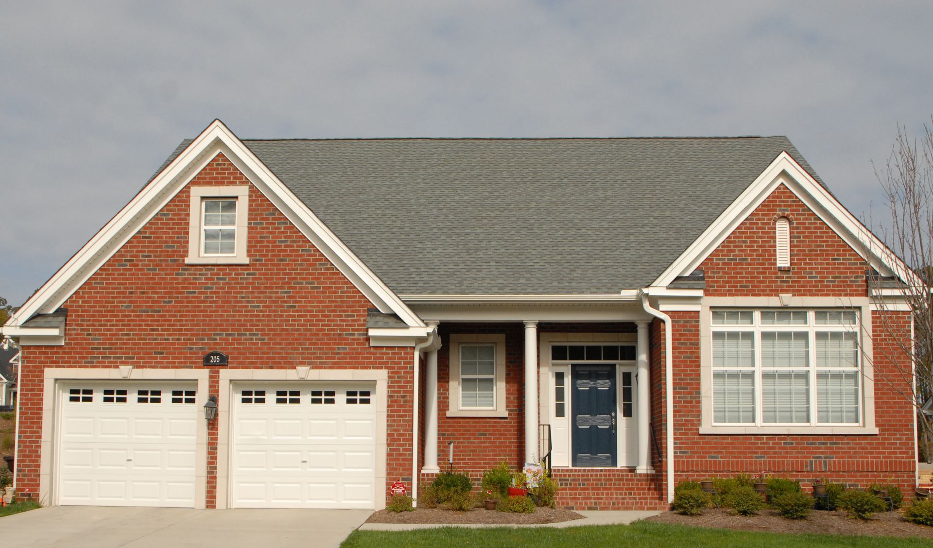Red brick house with white trim, gray roof, and two-car garage. Blue front door and windows.