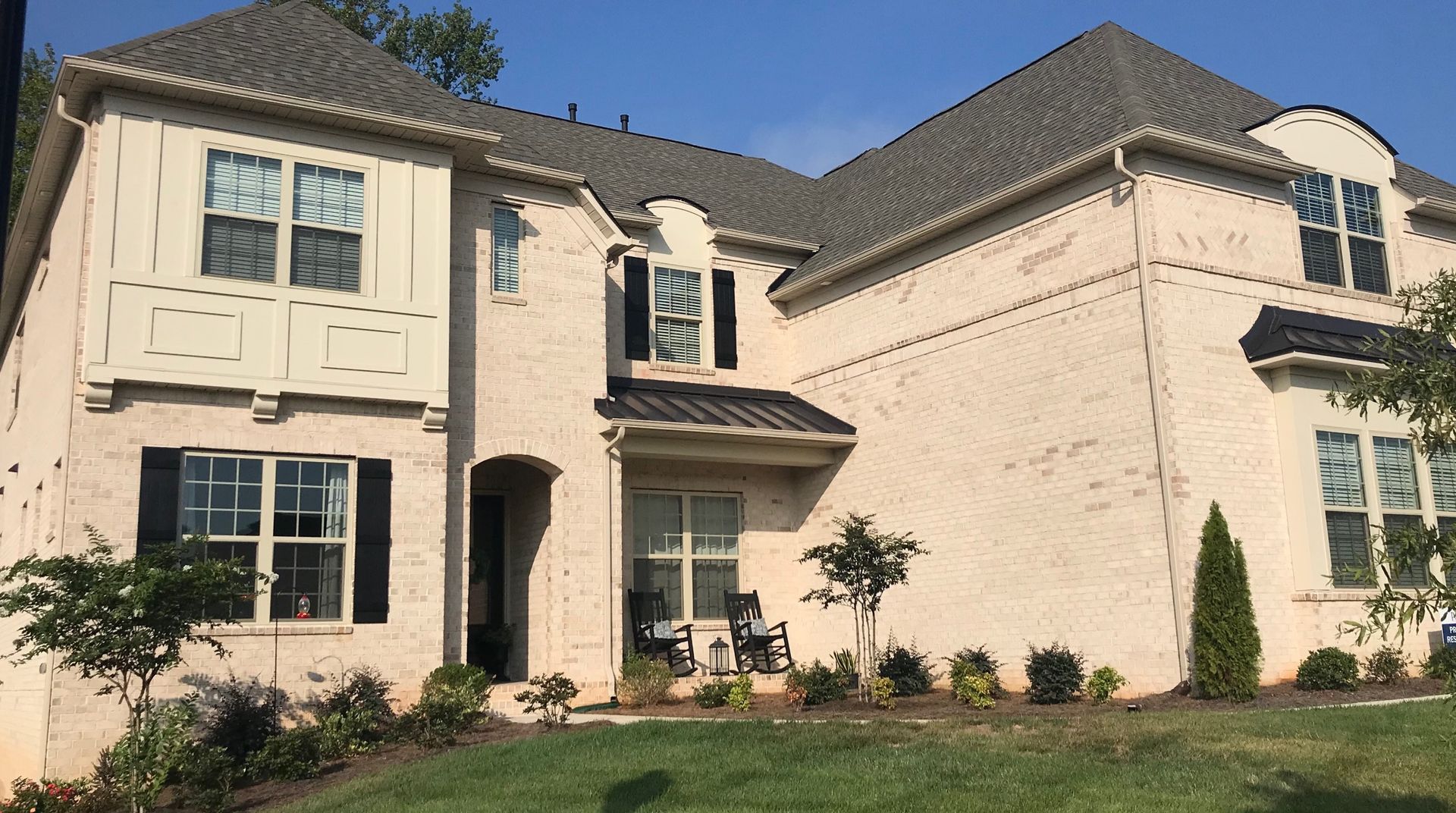 Two-story brick house with black shutters and a gray roof. Landscaped front yard.