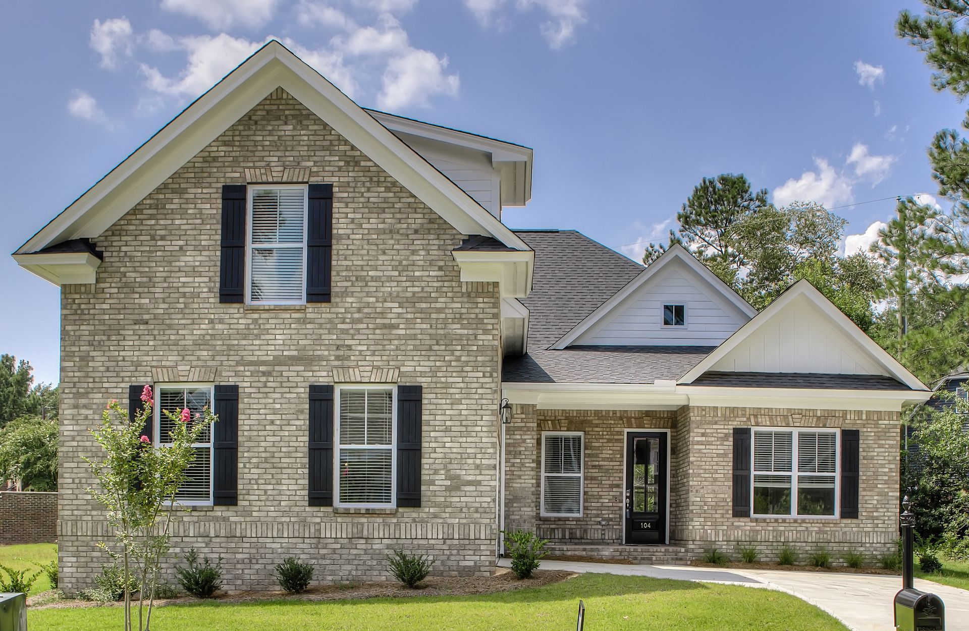 Beige brick two-story house with black shutters, white trim, and a small front yard.