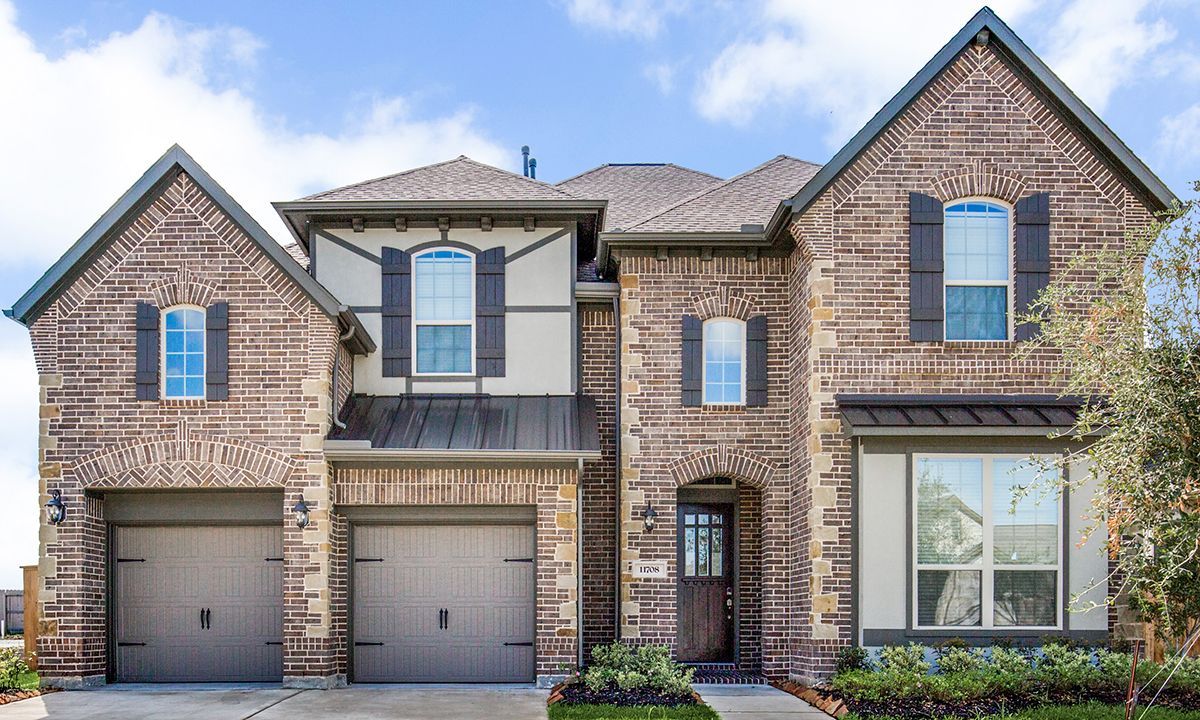 Two-story brick house with a brown door, garage, and blue sky background.
