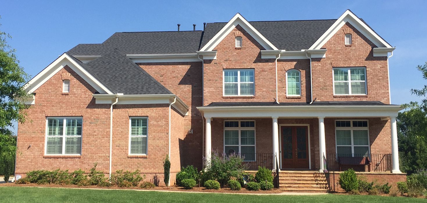 Brick house with white trim, dark roof, front porch, and manicured lawn.
