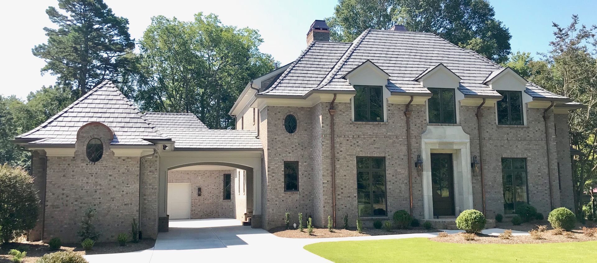 Large brick house with a tiled roof, carport, and manicured lawn.