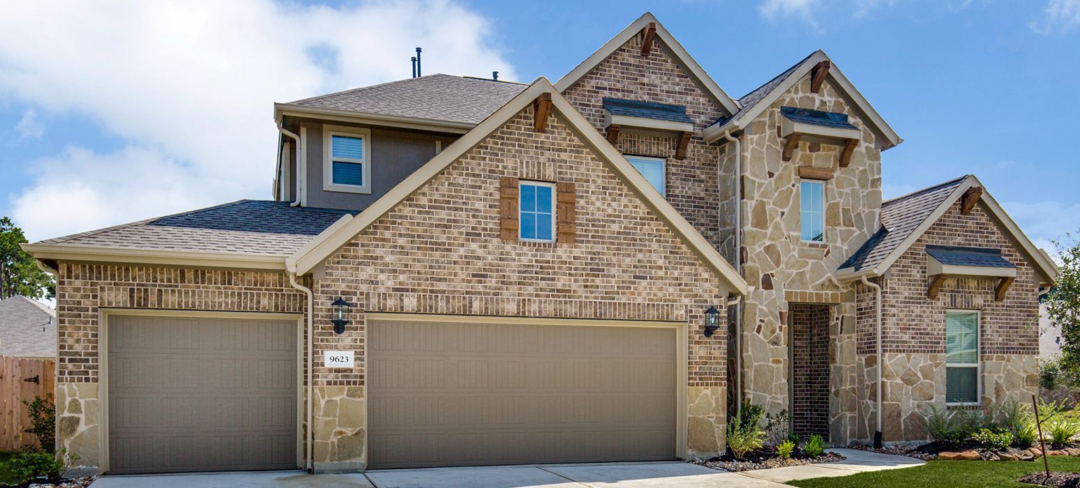 A two-story house with brick and stone exterior, two garage doors, and a blue sky in the background.