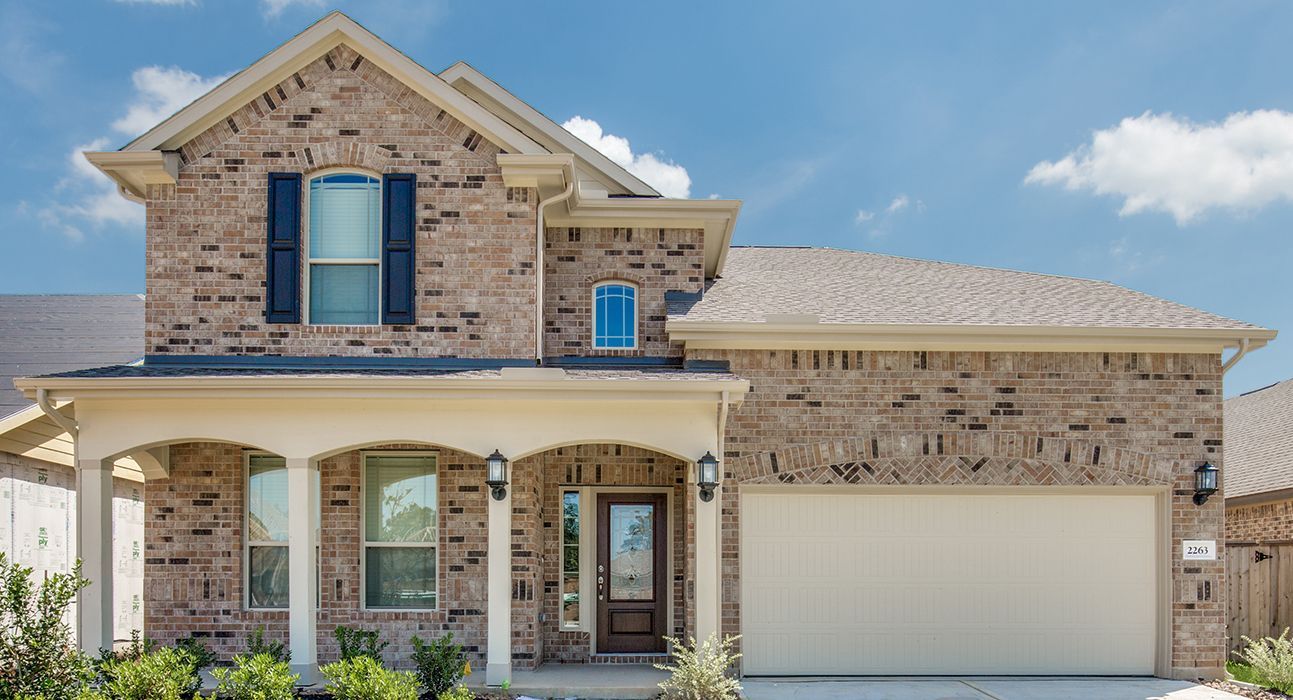 Two-story brick house with a front porch, garage, and blue sky.