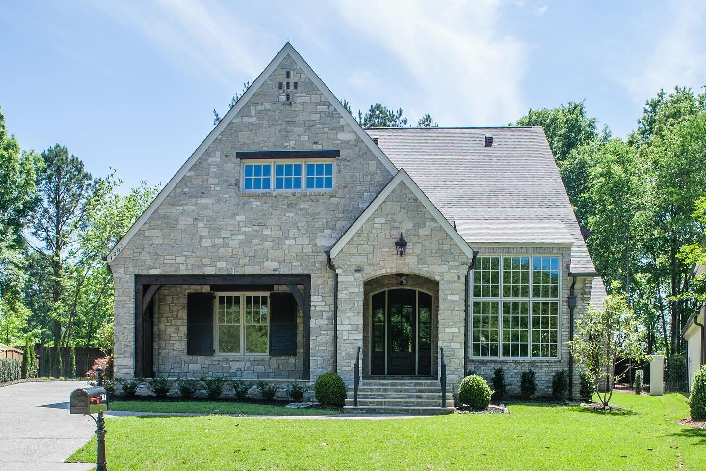 Stone house with a steeply pitched roof, large windows, and manicured lawn on a sunny day.