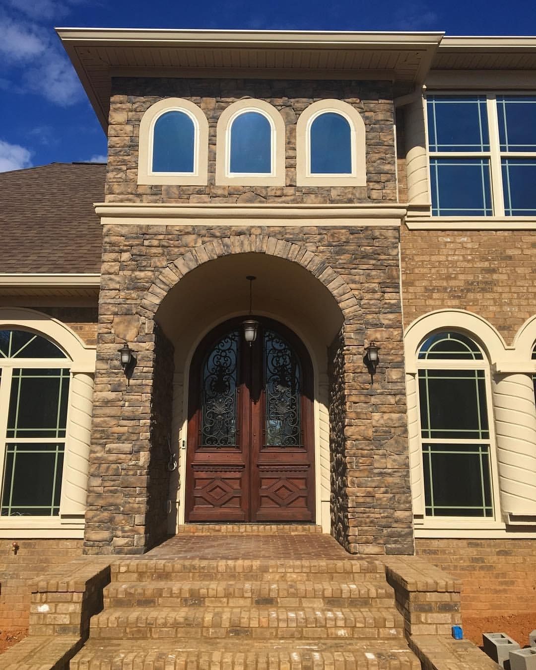Stone facade entrance with arched doorway, double doors, arched windows, and steps.