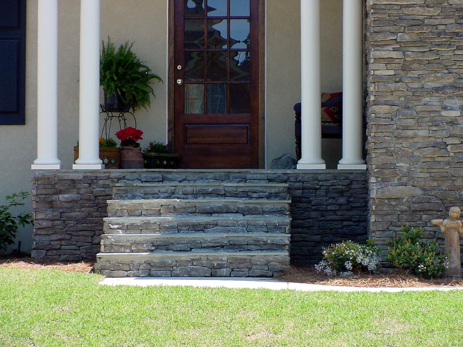 Stone steps leading to a front porch with columns, a dark wooden door, and stone facade.