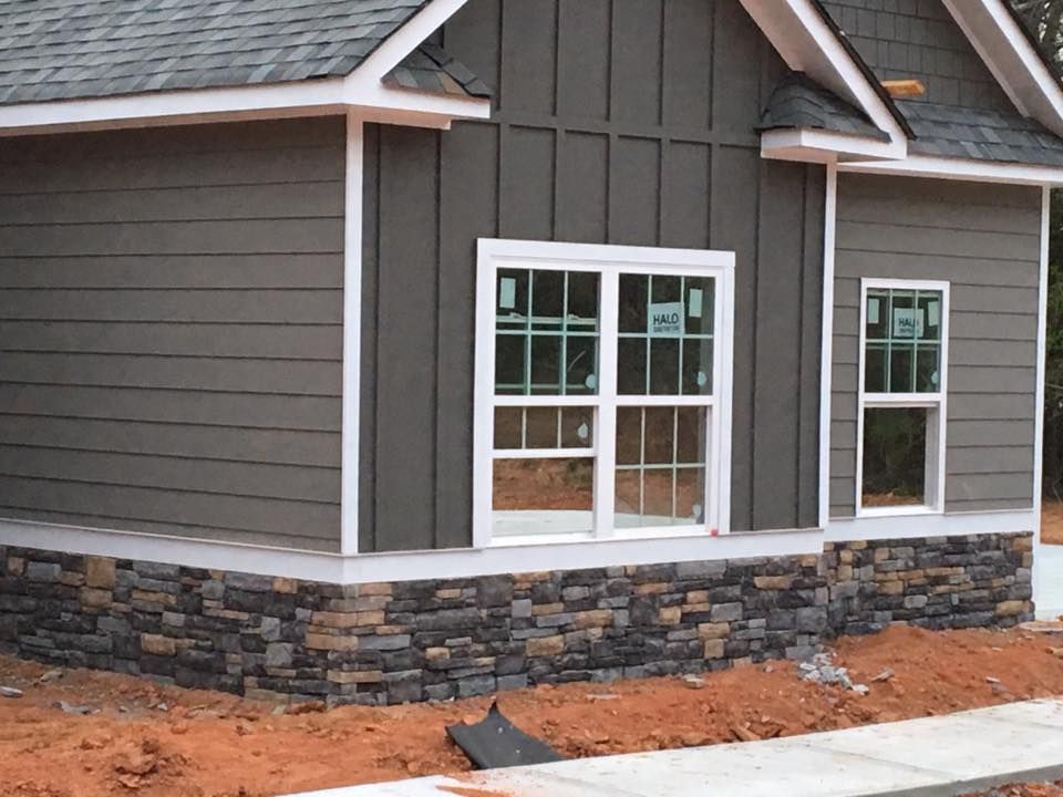 House exterior with dark gray siding, stone base, and white-framed windows.
