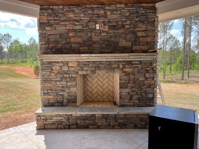 Stone fireplace with herringbone brick interior, set on a patio with a natural landscape.