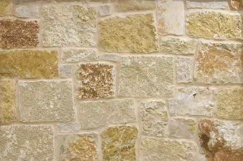 Stone wall with various beige, tan, and brown blocks and light mortar.
