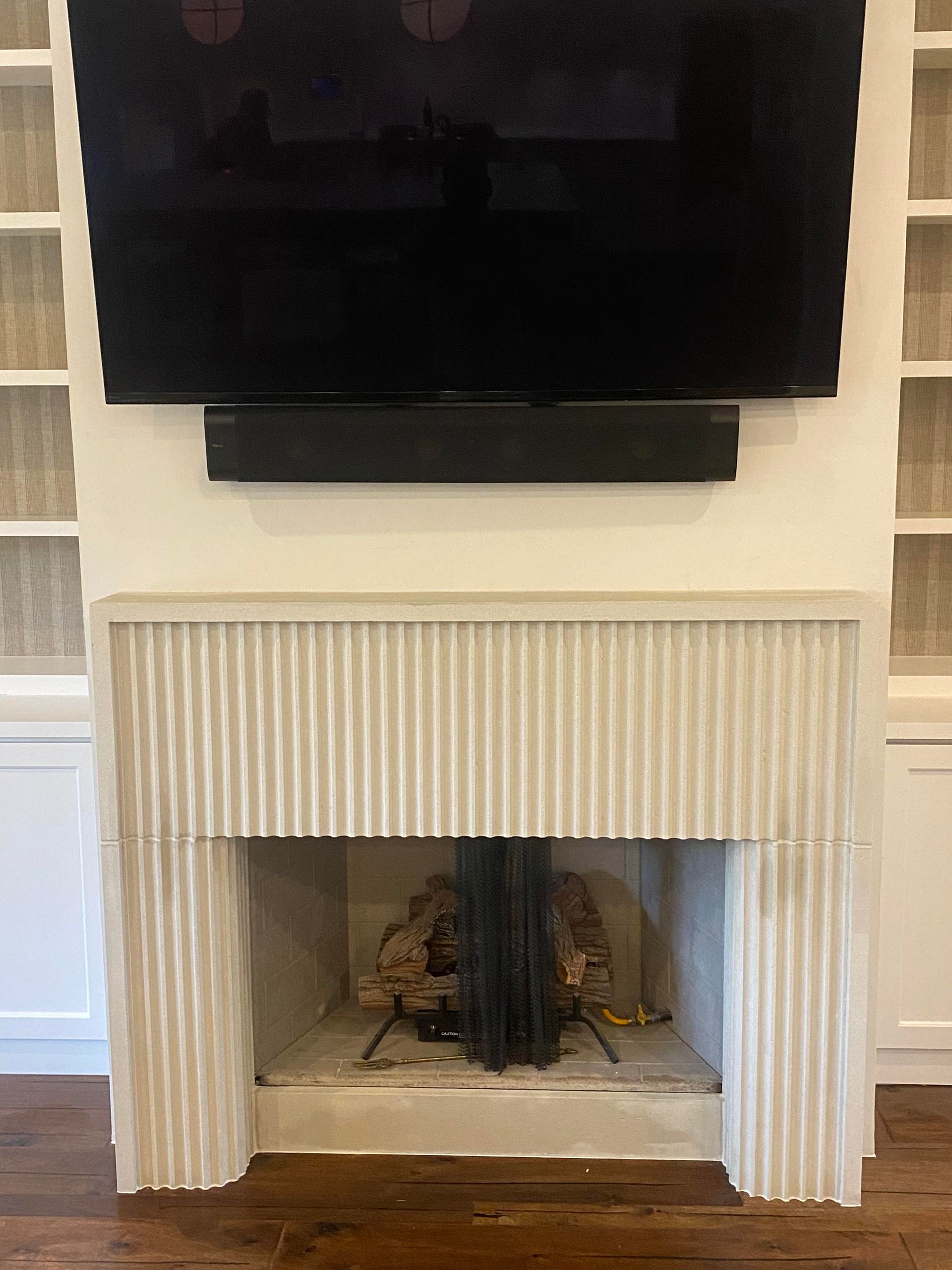 Fireplace with TV mounted above, flanked by built-in shelves. Beige and white tones dominate the setting.