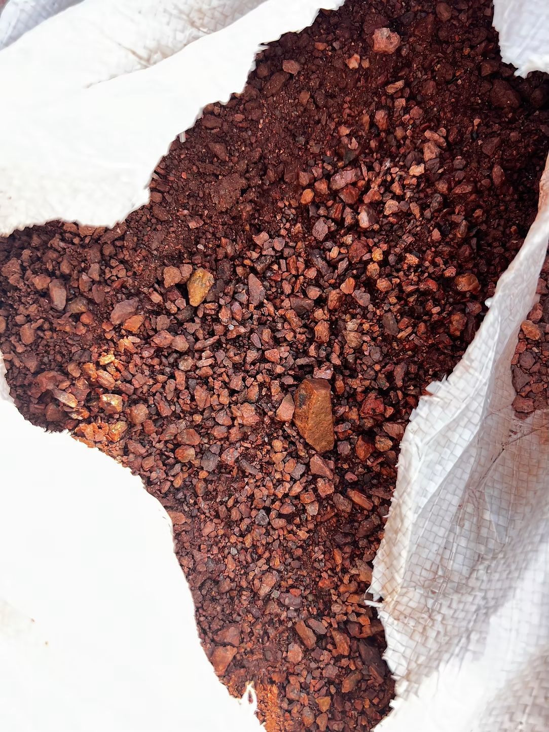 Red-brown, chunky soil fills a white bag, top-down view.