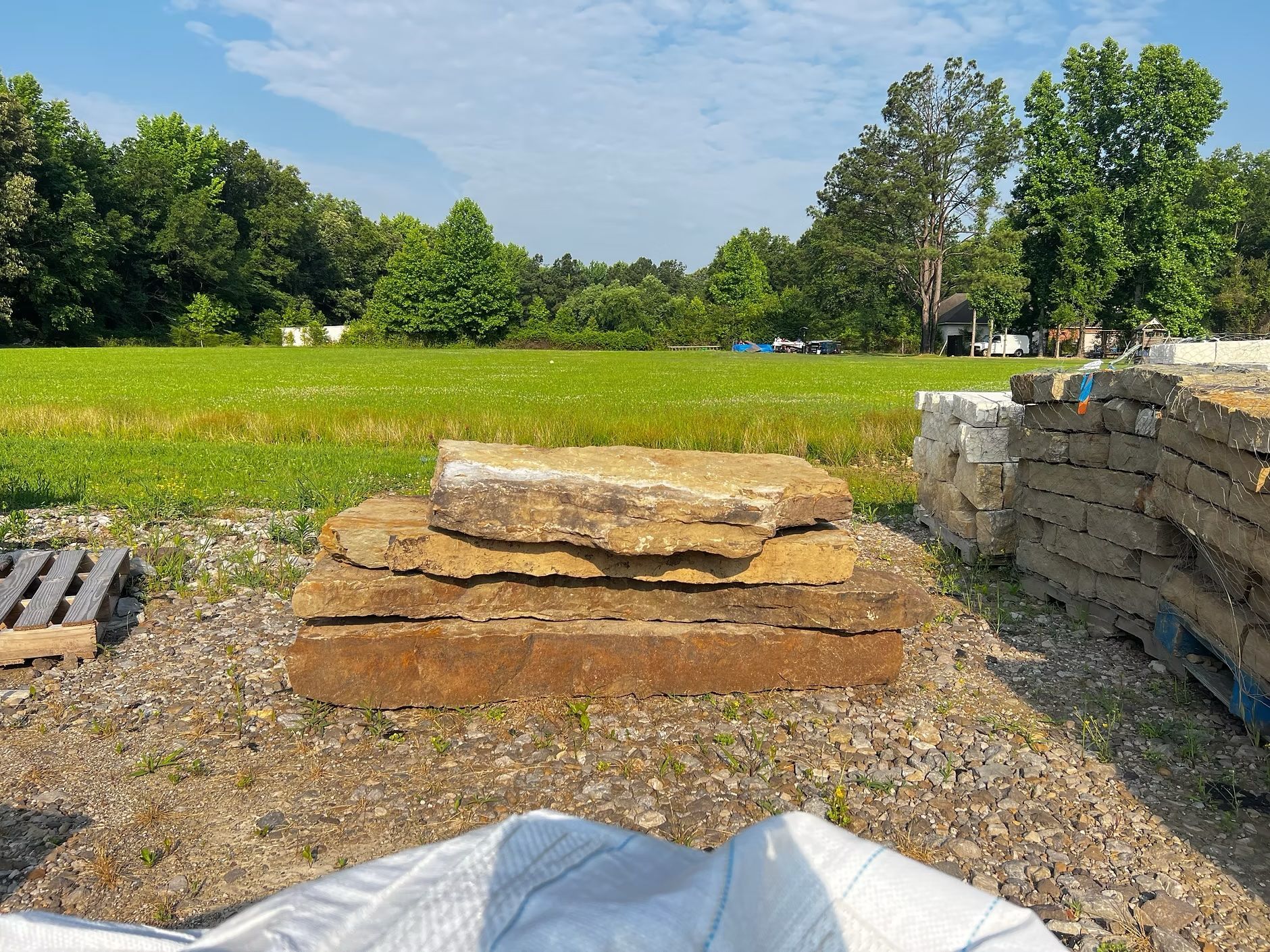 Stack of brown flagstones in a grassy field with trees under a blue sky.