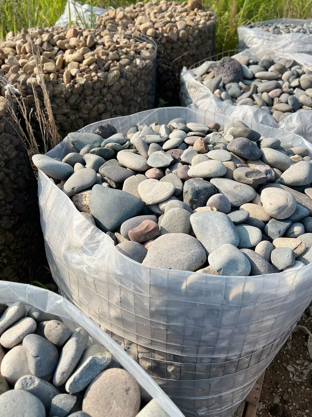 Bags of various sized river rocks, in shades of gray, brown, and blue, ready for landscaping use.