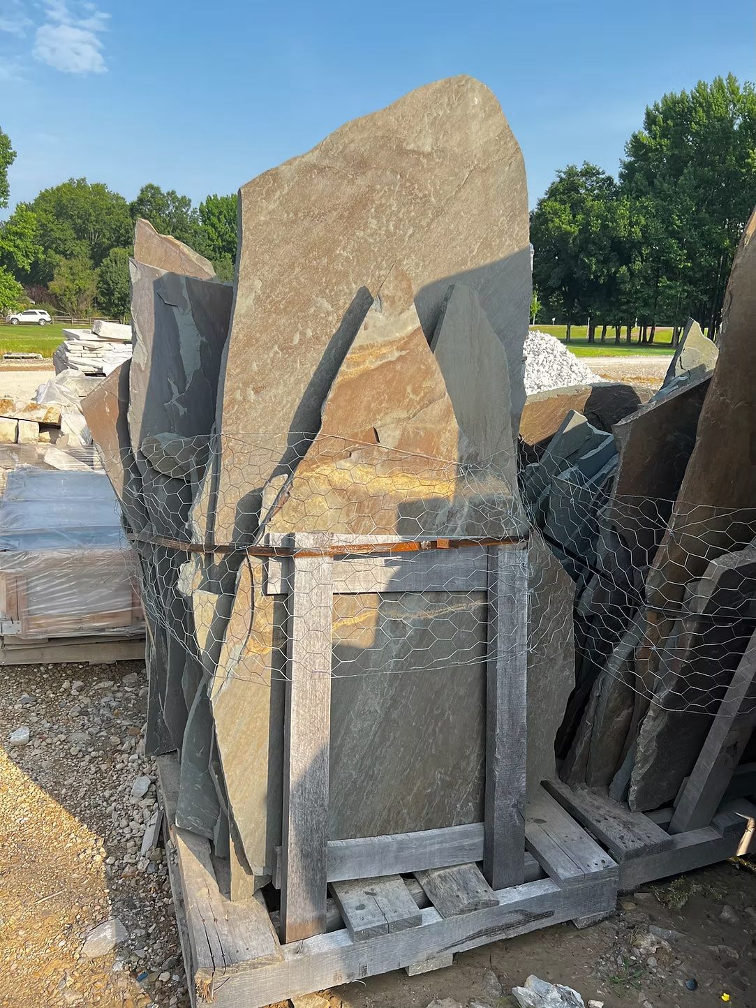 Bundle of large, irregular gray and brown stone slabs tied together on a wooden pallet. Outdoors, sunny day.