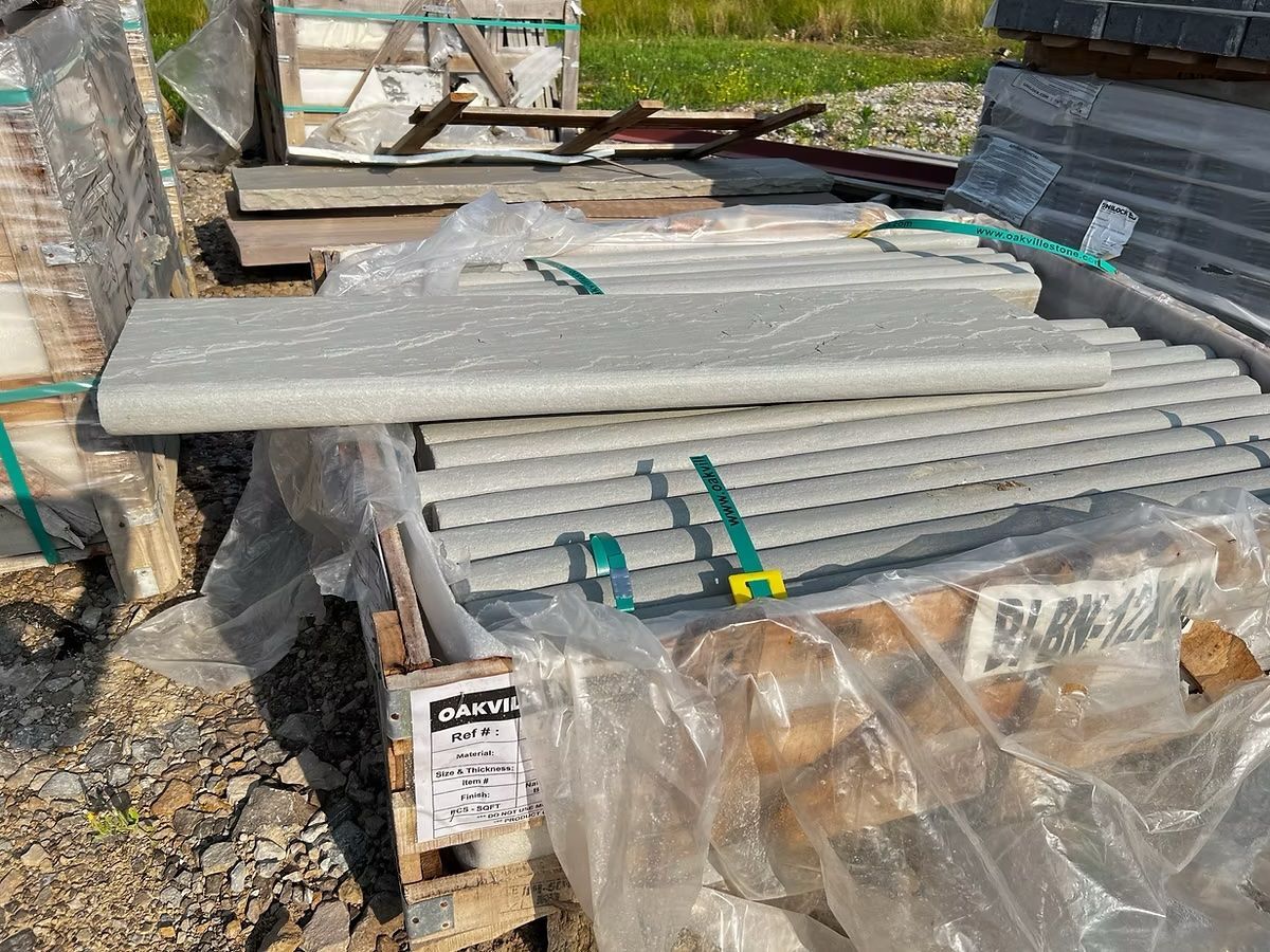Pallet of construction materials wrapped in plastic, including long, gray stone pieces and cylindrical elements.