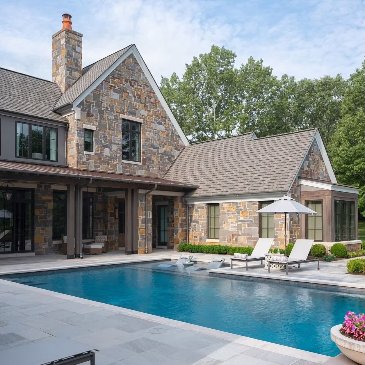 Stone house with a pool. Two lounge chairs under an umbrella by the pool.