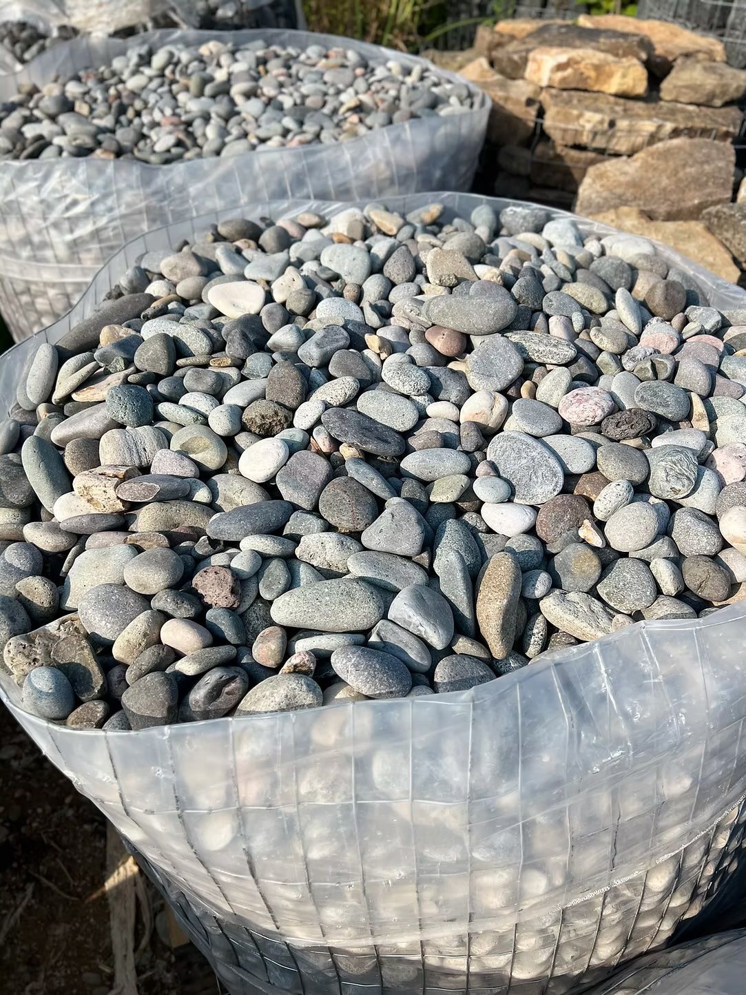 Bags filled with a variety of small, rounded gray and tan river rocks.