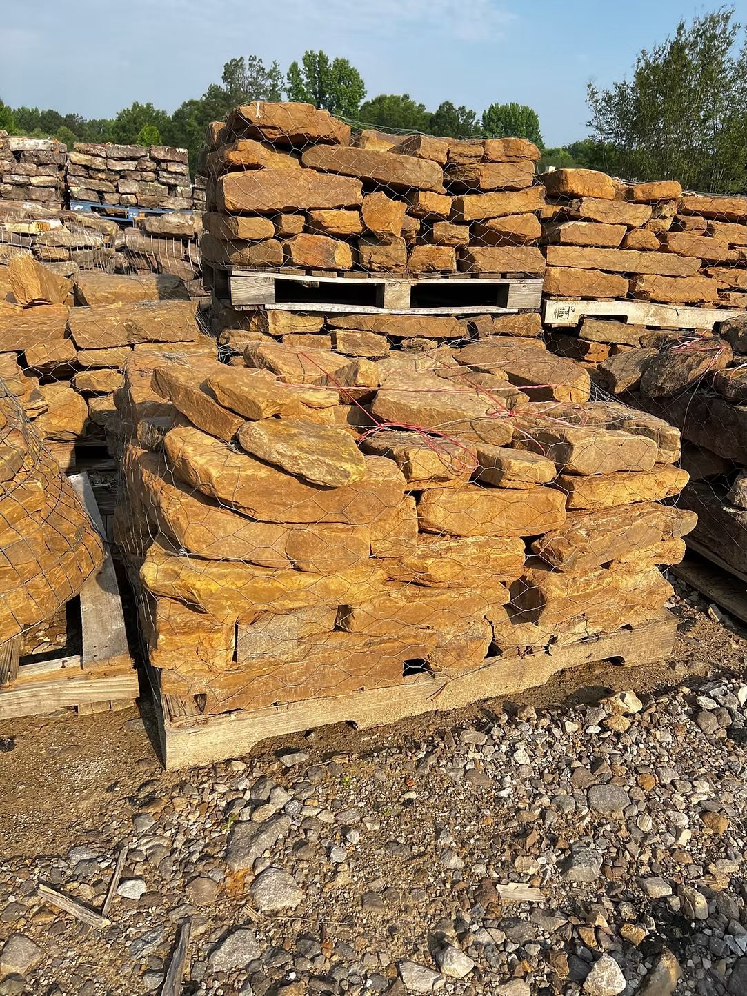 Stacks of rough, tan-colored rectangular stones on wooden pallets outdoors.
