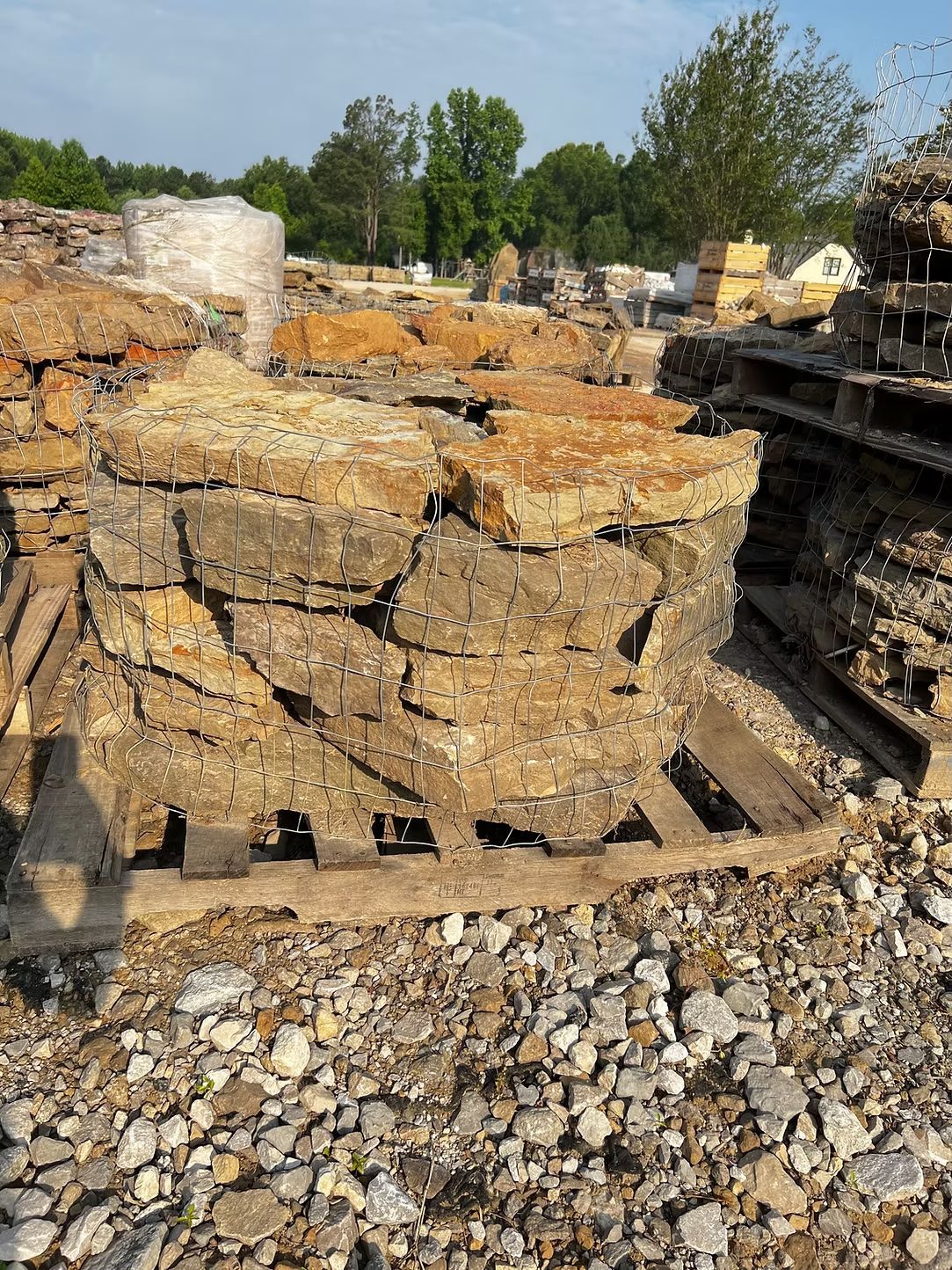 Stacks of weathered stone slabs on wooden pallets at an outdoor materials yard.